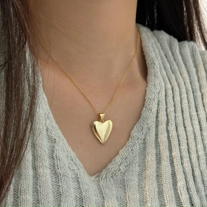 Close-up of a high-polished golden heart pendant necklace worn on a grey sweater