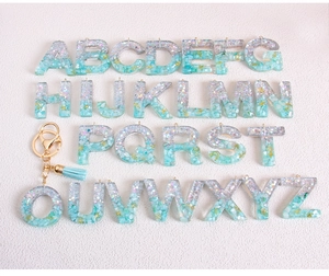 Macro shot of 26 resin glitter alphabet charms with blue-green gradient and golden sequins