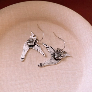 Gros plan détaillé des boucles d'oreilles colibri rétro avec gravure florale sur plateau