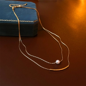 Detail of double-layer gold necklace with baroque pearl and curved metal bar pendant