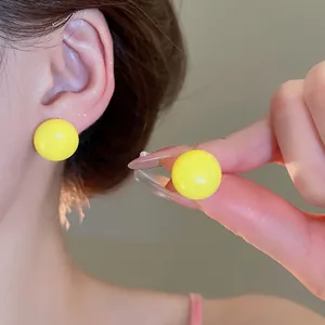 Minimalist bright yellow spherical stud earrings with a glossy finish on ear and hand