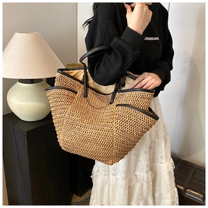 Detail of handwoven straw tote with black leather trim and dual handles for beach vacation
