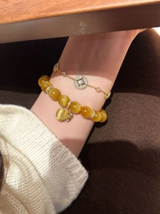Close-up of 18K gold plated star bracelet paired with amber beads and lucky bag charm