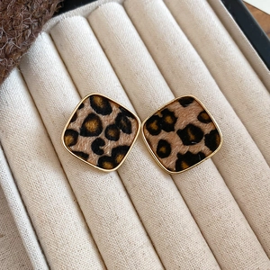 Macro view of leopard print square stud earrings with golden metal frame on velvet