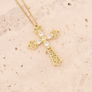 Macro shot of 18K gold plated cross pendant with cubic zirconia on a stone surface