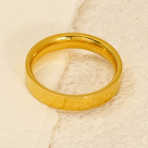 Detail view of a minimalist golden stainless steel ring on beige textured paper
