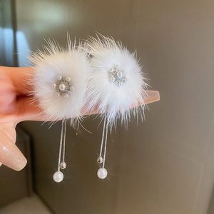 Close-up of white plush pompom earrings with pearl dangles and rhinestone accents