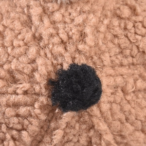 A close-up detail of the soft brown sherpa fleece material with a black plush pom-pom accent