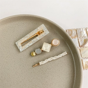 Detail shot of three pearl hair clips with resin and gold accents on a ceramic dish