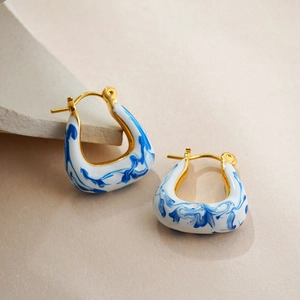 Detailed view of 18K gold hoop earrings with blue and white enamel marble texture