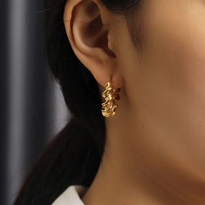 Close-up of a woman wearing gold twisted hoop earrings with a chunky spiral texture
