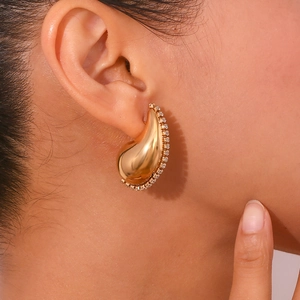 Gros plan de boucles d'oreilles goutte dorées avec cristaux portées par une femme