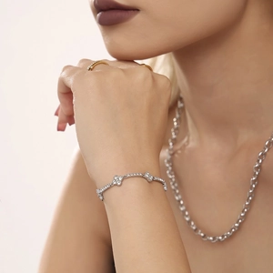 Elegant silver clover bracelet with sparkling zircon set, worn with gold rings on model