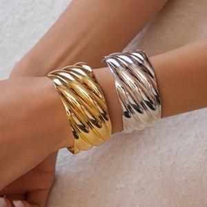 Detail showing wavy textured wide cuff bracelets in shiny gold and silver finishes