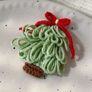 Close-up of a green knitted Christmas tree hair clip with a red bow on a white plate