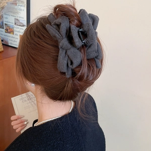 Close-up of a large dark grey fabric bow hair claw clip worn on a model back view