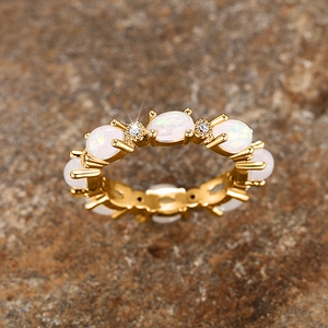 Gros plan d'une bague dorée avec opales blanches et diamants sur fond de roche naturelle