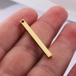 Polished gold rectangular bar pendant in stainless steel held on a fingertip