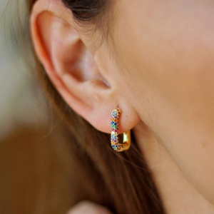 Close-up of golden U-shaped earrings with colorful rainbow zircon stones on model ear