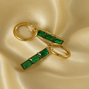 Détail de boucles d'oreilles créoles dorées 18K avec trois pierres de zircon vert émeraude