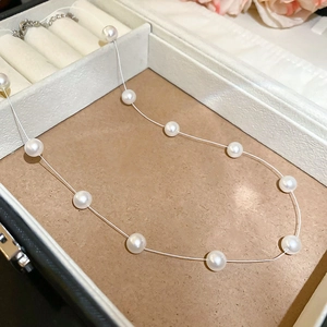 Détail d'un collier de perles blanches avec chaîne réglable dans un écrin en velours blanc