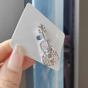 Detail of silver violin brooch with clear rhinestones held against a display card