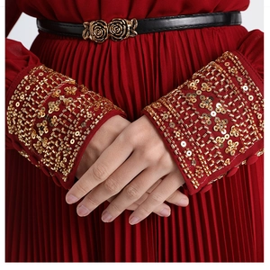 Close-up of red pleated dress featuring gold sequin beadwork cuffs and floral belt buckle