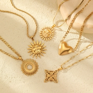 Five gold-plated sun and heart pendants with varied chains on a minimalist stone background