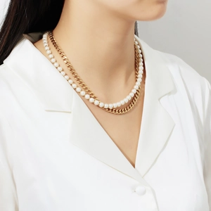 Close-up of layered 18K gold-plated Cuban chain and white pearl necklace on model