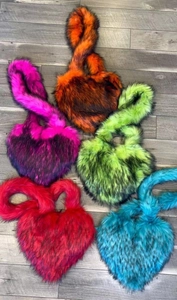Detailed flat lay of heart shaped faux fur bags in five vibrant neon colors on wood floor
