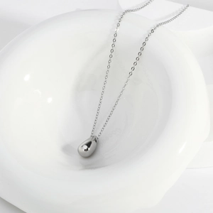 Macro shot of mirror-polished silver teardrop pendant necklace with minimalist fine chain link