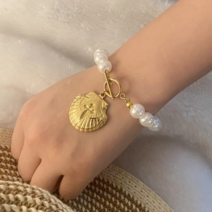 Golden seashell charm and large white pearl bracelet on wrist with T-bar clasp detail