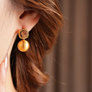 Detail of elegant gold earrings with square dark texture and matte sphere drop on model