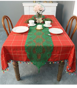 Detail of green lace table runner over red plaid cloth with festive colorful tassels