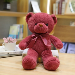 Lindo oso de peluche rojo oscuro con lazo de cinta a juego en un ambiente acogedor
