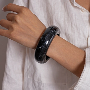 Detail of wide resin bangle with black and white marble pattern worn on a model's wrist