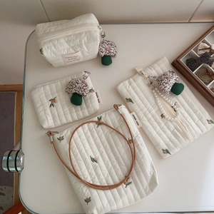 Detailed view of cream quilted cotton bags with orange embroidery and pearl handle