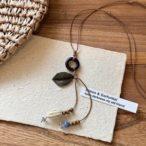 Close-up of bohemian ceramic pendant with wooden beads and bronze leaf on woven cord