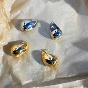 Detailed macro view of gold and silver teardrop earrings on beige textured background