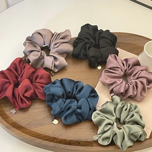 Close-up of premium satin scrunchies in six colors with metal charms in a wooden tray