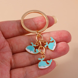 Détail de porte-clés doré avec pendentifs baleine émaillés bleu et blanc tenu à la main