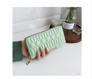 Detail of mint green quilted PU leather wallet with zipper closure held by a model