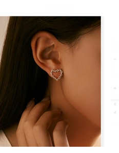 Close-up of a heart-shaped chain stud earring in silver on a model's ear