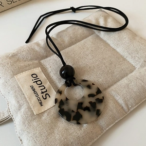 Detailed close-up of hollow resin pendant necklace with beige linen jewelry storage pouch