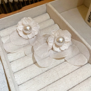 Detailed close-up of ivory fabric flower earrings with center pearl in a beige jewelry box