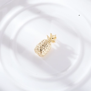 Macro shot of a gold-plated pineapple pendant charm on white textured ceramic surface