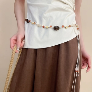 Detail of beaded tassel waist chain featuring amber and cream resin beads on a brown skirt