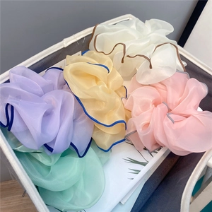 Five oversized pastel organza scrunchies in a grey storage basket from an overhead view