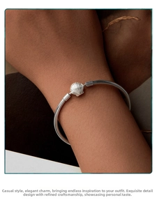 Close-up of a silver open cuff bracelet featuring a detailed seashell design on a wrist