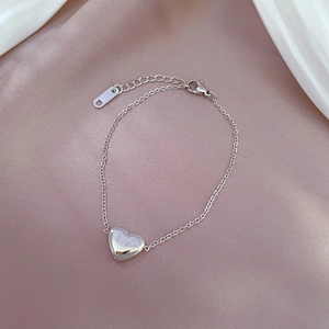 Detail of silver heart charm bracelet with adjustable chain on elegant silk fabric